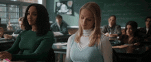a girl in a blue sweater sits in a classroom with other girls