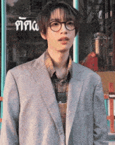 a young man wearing glasses and a suit stands in front of a window that says ' a '