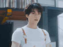 a young man wearing a white t-shirt and brown suspenders looks surprised .