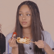 a woman with dreadlocks is eating a hot dog on a stick ..