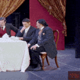 a group of men sit at a table with a red curtain behind them and a sign that says vto