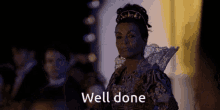 a woman in a fancy dress is standing in front of a crowd and says well done .