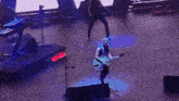 a man is playing a guitar on stage while another man stands behind him .