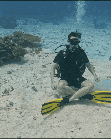 a scuba diver wearing a black shirt and black shorts is sitting on the sand