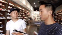 two men are standing in a shoe store and one is holding a pair of shoes