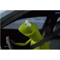 kermit the frog is driving a car and looking out the window .