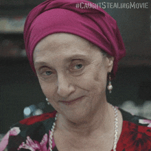 an older woman wearing a purple head scarf and pearl earrings is smiling for the camera