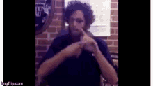 a man with curly hair is sitting in front of a brick wall making a funny face .