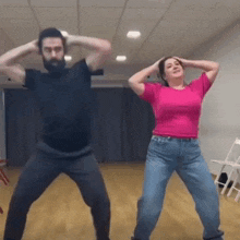 a man and a woman are dancing together in a room . the woman is wearing a pink shirt .