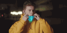 a young man wearing a yellow hoodie is putting on a blue light up mask .
