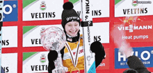 a woman holding a trophy in front of a wall that says veltins on it