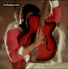 a man in a red shirt is holding a red guitar .