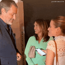 a man in a suit is talking to two women in front of a sign that says say.org