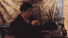 a man is playing a guitar in front of a wall with a floral tapestry behind him