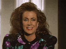 a woman wearing a purple and black floral dress smiles for the camera
