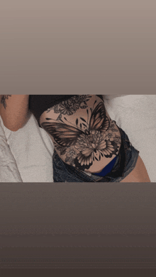a woman laying on a bed with a butterfly tattoo on her stomach