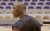 a man is standing on a basketball court in front of a row of empty seats .