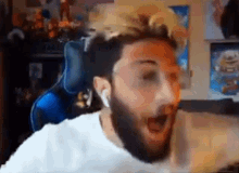 a man with a beard is sitting in front of a computer with his mouth open and headphones on .