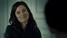 a woman in a blue shirt smiles while looking at another person