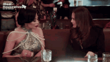 two women are sitting at a table in front of a sign that says " real housewives "