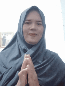 a woman wearing a blue hijab holds her hands together in prayer