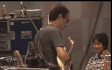 a man is playing a bass guitar in a band while another man plays drums .