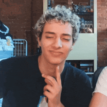 a man with curly hair is making a funny face with his finger on his chin