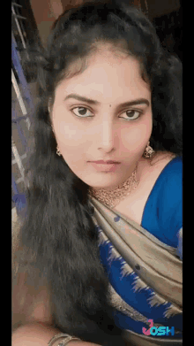 a woman wearing a blue top and a gold necklace is taking a picture of herself