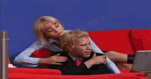 a woman is sitting on a man 's back in a red chair with a laptop .