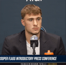 a man in a suit is talking into a microphone with the words cooper flagg introductory press conference below him