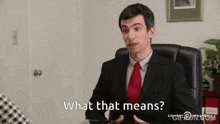a man in a suit and tie is sitting at a desk and says what that means