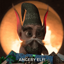 a cartoon elf with a hat and a beard is holding a gift box and says " angery elf "