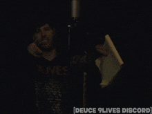 a man in an olive shirt is standing in front of a microphone in a dark room