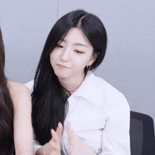 a woman with long black hair is wearing a white shirt and earrings and making a funny face .