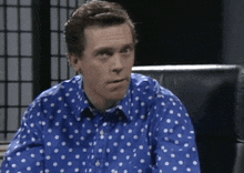 a man wearing a blue shirt with white polka dots is sitting in a chair
