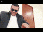 a man wearing sunglasses and a white shirt is pointing to the camera