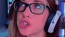 a woman wearing glasses and headphones is sticking her tongue out while making a funny face .