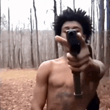 a man without a shirt is pointing a gun at the camera in the woods .