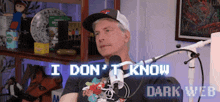 a man sitting in front of a microphone with the words i don 't know dark web written on the screen behind him