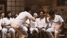 a group of men in white shirts are sitting around a man in a white shirt with a yellow badge on his chest
