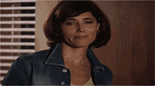a woman wearing a denim jacket and a yellow tank top smiles