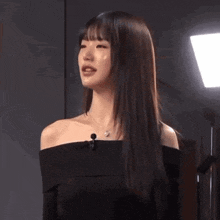 a woman with long dark hair is wearing a black off the shoulder top and a necklace .
