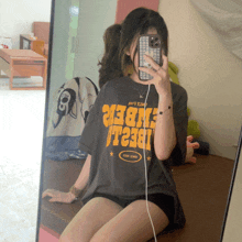 a girl taking a selfie in front of a mirror wearing a t-shirt that says amber