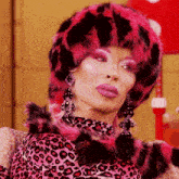 a drag queen wearing a pink and black fur hat and earrings
