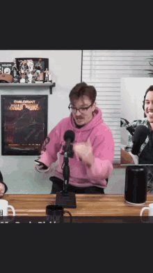 a man in a pink hoodie stands in front of a microphone in a room