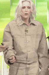 a blonde woman wearing a tan jacket and pants