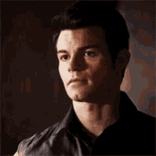 a man in a black shirt and leather vest is smiling and looking to the side .