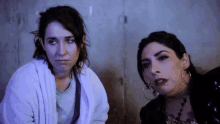 two women are sitting next to each other and one has a tattoo on her chest