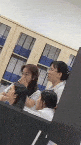 a group of women are sitting around a desk with binders on the shelves behind them
