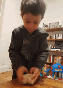 a young boy in a black jacket is kneading dough on a wooden table